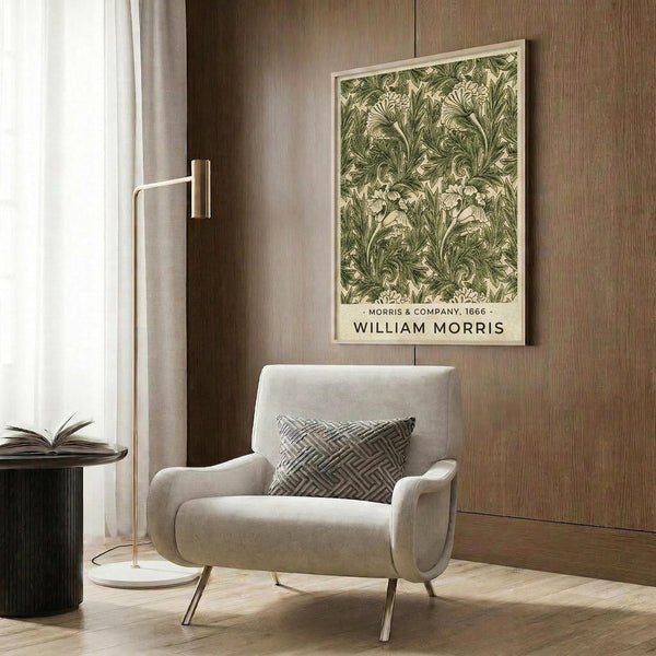 May include: Framed botanical print with intricate green acanthus leaf pattern on cream background, displayed on wood paneled wall above beige upholstered armchair with geometric throw pillow. Modern brass floor lamp and side table with open book complete the neutral-toned reading nook with curtained window.