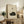 May include: Framed beige poster with black illustration of sleeping curled cat and Japanese characters, displayed on rustic wooden sideboard next to fern plant, books, ceramic vase, and brown leather chair in warm-toned living room with white walls