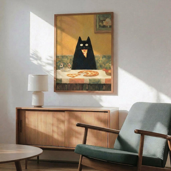 May include: Framed artwork showing a large black cat with bright yellow eyes sitting at a white table with pizza and teapot, displayed above a wooden sideboard with white lamp in a mid-century modern living room with sage green armchair and natural lighting creating shadows on white walls.