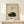 May include: Framed vintage-style poster featuring a curled black cat sleeping peacefully with Japanese calligraphy characters above, displayed on light wood shelf next to small white wrapped gift with evergreen sprig. Cream textured background, natural wood frame, minimalist styling.