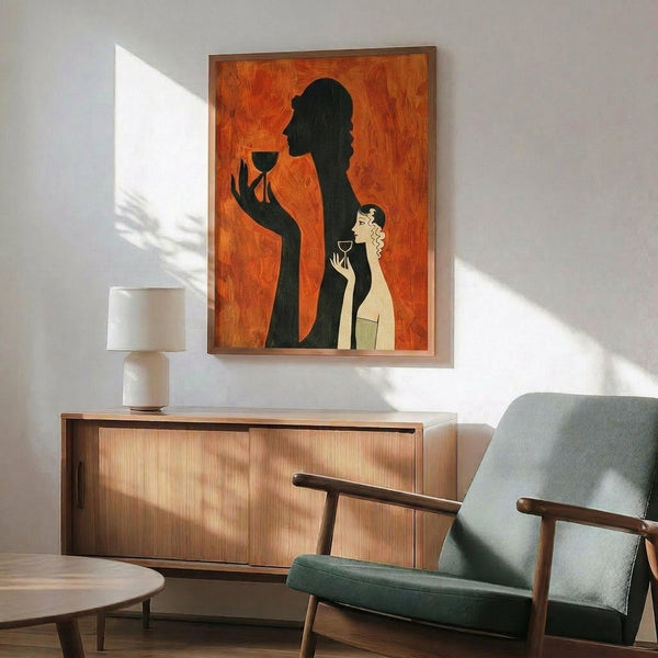 May include: Framed art print on white wall showing orange background with black silhouette of elegant woman holding wine glass and smaller light-colored figure also with glass. Wood-framed poster hangs above mid-century modern walnut credenza with white ceramic lamp. Sage green upholstered chair with wooden arms sits nearby on hardwood floor with natural sunlight creating dramatic shadows across the minimalist living room scene.