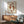 May include: Framed poster featuring two orange-red koi fish arranged in circular yin yang formation on cream background, displayed above mid-century modern walnut credenza with white ceramic lamp, next to sage green upholstered armchair with wooden frame, warm sunlight casting shadows across white wall in minimalist living room setting