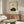 May include: A framed vintage Japanese-style poster featuring a curled up sleeping black cat with Japanese calligraphy text on cream background, displayed above a mid-century modern walnut credenza in a minimalist living room with white upholstered chair, oval glass coffee table, and warm natural lighting casting shadows across neutral walls.