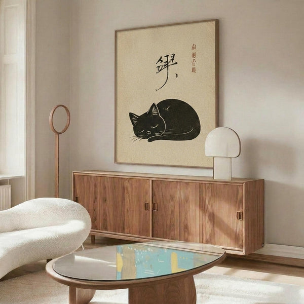 May include: A framed vintage Japanese-style poster featuring a curled up sleeping black cat with Japanese calligraphy text on cream background, displayed above a mid-century modern walnut credenza in a minimalist living room with white upholstered chair, oval glass coffee table, and warm natural lighting casting shadows across neutral walls.