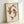 May include: Framed art print featuring two koi fish in reddish-brown ink forming a circular yin-yang pattern on cream textured paper. The fish show detailed scales and flowing fins, displayed in a light wooden frame leaning against a white wall with soft natural lighting creating shadows.