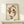 May include: Framed poster print featuring two rust-colored koi fish arranged in a circular, yin-yang pattern on cream textured paper background. Natural wood frame displayed on light wooden console table against white wall. Small white wrapped gift box with green sprig placed in front of frame. Warm natural lighting creates soft shadows.