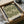 May include: Vintage botanical poster with intricate green acanthus leaf pattern on cream background, displayed in black frame inside brown cardboard packaging with tissue paper. The detailed Morris & Company 1866 design features ornate flowing foliage in sage green tones. Package sits on white fabric surface alongside rolled paper tubes and dark glass vessel.