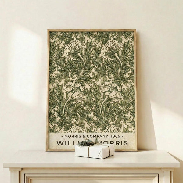 May include: Framed botanical poster with intricate green and cream acanthus leaf pattern in ornate Victorian style, displayed on light wood console table with small wrapped gift box beside it against neutral wall