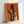 May include: Framed poster with orange textured background featuring black silhouette of elegantly dressed figure holding wine glass, alongside smaller light-colored woman with curly hair also holding glass. Art deco style artwork in light wooden frame, leaning against white wall corner showing perspective and shadow.