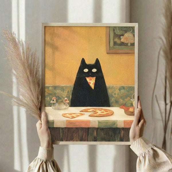 May include: Hands holding a framed art print featuring a black cat with glowing yellow eyes sitting at a table with pizza slices. The illustration shows a cozy interior with yellow walls, decorative elements, and warm lighting. The frame appears silver or light colored, and dried pampas grass is visible to the left against white curtains in the background.