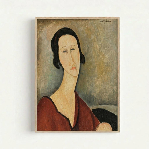 Framed reproduction of a Modigliani portrait showing a woman with elongated features, dark bobbed hair, and wearing a deep red v-neck garment. The painting displays the artist's characteristic style with a pale, oval face, almond-shaped eyes, and muted earth-tone background. The artwork is displayed in a light wooden frame against a white wall.