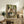 May include: Framed art print of ballet dancers in white tutus with green sashes practicing in an ornate studio with pale green walls and large mirror. Print displayed on rustic wooden sideboard alongside decorative pottery, books, fern plant, and cream upholstered chair with brown leather pillow visible in foreground.