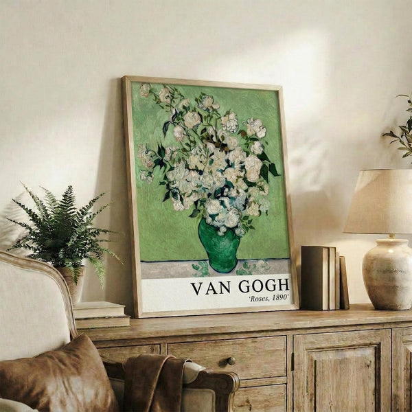 May include: Framed Van Gogh Roses poster with white flowers in green vase against pale green background, displayed on rustic wooden sideboard alongside fern plant, ceramic vases, and books in neutral-toned living room with beige chair and white walls