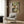 May include: Framed reproduction of Edgar Degas ballet painting showing dancers in white tutus with green sashes in a rehearsal room, displayed on wood-paneled wall above beige upholstered chair with geometric pillow, modern floor lamp and side table with open book nearby