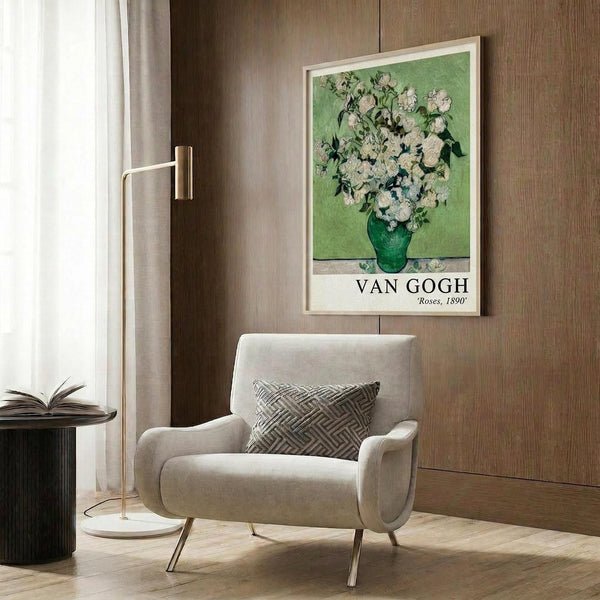 May include: Van Gogh roses poster in light wooden frame hanging on wood-paneled wall above beige upholstered armchair with geometric pillow. Modern floor lamp with brass finish stands nearby next to dark round side table with open book. Poster shows white and pink roses in green vase against mint green background with artist name and date below.