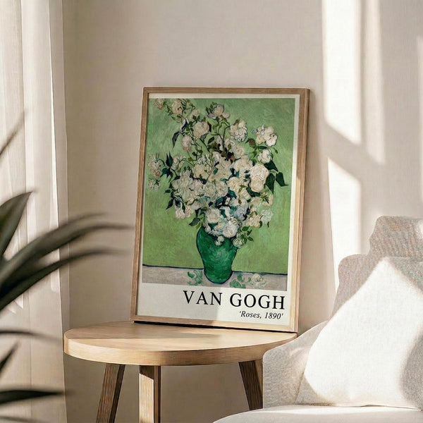 May include: Framed art print of white roses in a green vase against a light green background, displayed on a round wooden side table next to a beige upholstered chair. Natural sunlight creates shadows on the cream colored wall. The vintage-style botanical artwork features thick brushstroke textures and is matted in white with wooden frame.