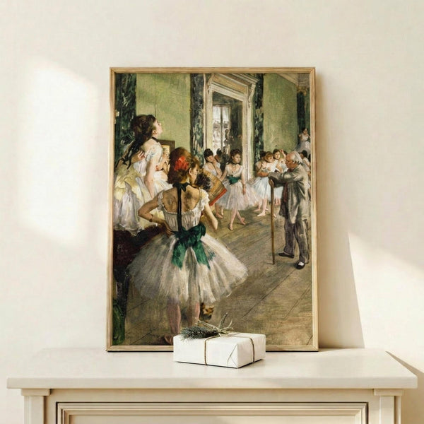 May include: Framed reproduction of Degas ballet painting showing young dancers in white tutus with green sashes practicing in an ornate room with green walls, displayed on light wood surface beside small white wrapped gift with evergreen sprig against cream wall