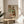 May include: Framed art print featuring two embracing figures in expressionist style with earthy tones of red, green, and brown, displayed on a round wooden side table next to a beige upholstered chair in a bright, minimalist room with white walls and natural lighting from a window.