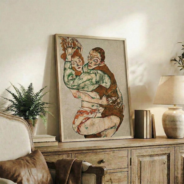 May include: Framed reproduction of an expressionist artwork showing two embracing figures in earthy tones of green, brown, and red, displayed on a rustic wooden sideboard alongside books, a ceramic vase, and a potted fern in a neutral-toned living room setting.