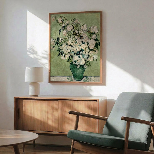May include: Van Gogh roses painting reproduction in wooden frame hanging above mid-century modern wooden credenza with white lamp, next to teal upholstered armchair with wooden arms. Artwork shows white and pink roses in green vase against sage green background. Warm sunlight creates dramatic shadows across white wall in styled living room setting.
