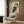 May include: Japanese woodblock print of an owl with detailed brown, teal and cream feathers displayed in silver frame on wood-paneled wall above beige upholstered chair with geometric patterned pillow, next to brass floor lamp and dark round side table with open book