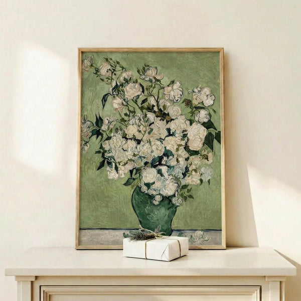 May include: Framed reproduction of Van Gogh's white roses painting in golden wood frame, displayed on light wooden console table against cream wall. Green vase holds abundant white blooms with thick impasto brushstrokes. Small wrapped gift box sits beside frame. Soft natural lighting creates gentle shadows.