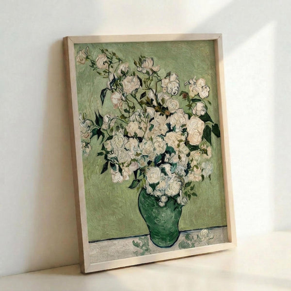 Framed reproduction of Van Gogh's roses painting featuring thick white blooms with green leaves in a dark green vase against a pale green background. The artwork displays characteristic impasto brushwork and Post-Impressionist style. Natural wood frame sits propped against white wall, showing the textured paint surface and vibrant color palette of greens and whites.