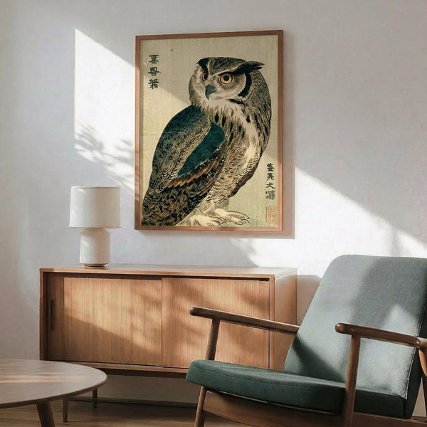 May include: Japanese woodblock print of an owl with brown and teal feathers and large orange eyes, displayed in a thin wooden frame above a mid-century modern wooden sideboard. A white ceramic table lamp sits on the credenza next to a teal upholstered armchair with wooden arms. Warm sunlight streams across the white wall creating geometric shadows in this contemporary living room setting.