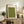 May include: Framed green textured artwork with minimalist bird silhouettes and vertical Japanese calligraphy text, displayed on rustic wooden sideboard alongside fern plant, ceramic vase, and books in neutral-toned living room setting with beige armchair