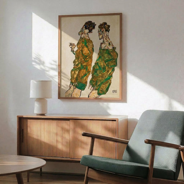 May include: Framed artwork showing two elongated figures in green and yellow robes with dark hair, displayed above a wooden sideboard with white ceramic lamp. Mid-century modern furniture including sage green upholstered chair with wooden arms. Warm sunlight creates geometric shadows on white wall, highlighting the expressionist-style drawing with its distinctive angular figures and earthy color palette.