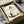 May include: Framed Japanese zen cat artwork displayed in cardboard packaging with protective wrapping. The minimalist ink brush painting shows a sleeping cat in black and gray tones with Japanese calligraphy characters above. Black frame sits in brown shipping box surrounded by white tissue paper, with wooden scroll tubes visible nearby and ink stone in background, creating an authentic Asian art presentation.