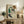 May include: Framed art print featuring a seated woman with reddish curly hair wearing a green sleeveless top and dark stockings, displayed on a rustic wooden sideboard alongside books, a small potted fern, and ceramic vase in a neutral-toned living room setting with cream upholstered furniture
