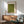 May include: Framed Japanese artwork with green textured background and three flying birds in black ink, displayed above a wooden sideboard with table lamp in modern living room setting with sage green upholstered chair and white walls with natural sunlight shadows.