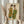May include: Person in cream outfit holding framed artwork showing two figures in flowing green and golden robes with dark hair, standing against neutral wall with dried wheat stems in other hand