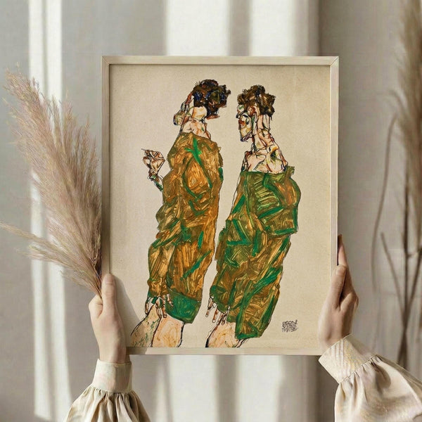 May include: Person in cream outfit holding framed artwork showing two figures in flowing green and golden robes with dark hair, standing against neutral wall with dried wheat stems in other hand