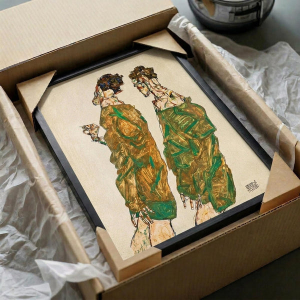 Framed art print of two figures in flowing green and gold robes with ornate headdresses, displayed in black frame inside cardboard shipping box with protective wrapping. The expressionist-style artwork shows elongated figures with detailed facial features and decorative clothing rendered in earthy tones on cream paper.