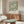 May include: Framed botanical poster with pink chrysanthemums, green leaves, and blue accents displayed above a walnut credenza in a modern living room. White curved chair and glass-top coffee table visible. Warm natural lighting creates shadows on cream walls.
