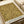 Ornate floral wallpaper pattern in golden yellow and brown tones featuring intricate Victorian-style botanical motifs with swirling vines, detailed flowers, and decorative leaves. The design sample is displayed on white paper with Morris & Company 1866 attribution text at bottom, photographed alongside rolled white papers on a neutral surface.