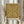 May include: Person in beige sweater holding framed poster featuring ornate golden botanical damask pattern with intricate leaves, flowers and symmetrical design. Dried pampas grass visible beside figure against soft neutral curtained background in natural lighting.