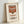 May include: Framed poster print of Campbell's tomato soup can in Andy Warhol pop art style, featuring red and white label design with vintage typography, displayed in light wooden frame against white wall with natural lighting creating soft shadows