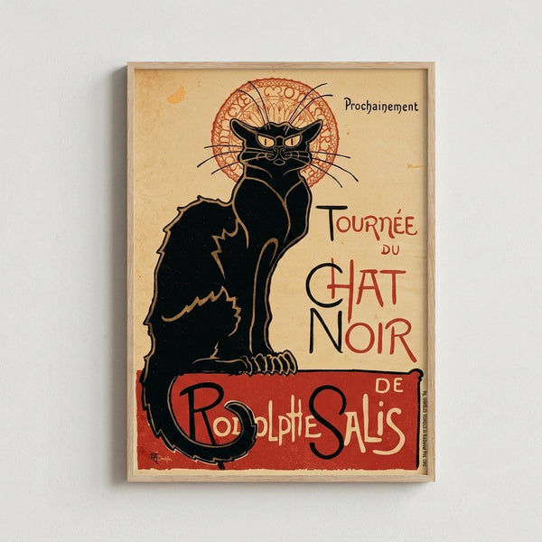 May include: Framed vintage French poster featuring a black cat with yellow eyes sitting upright against cream background. The cat has an ornate red circular halo or decorative element behind its head. Red and black French text reads "Tournée du Chat Noir" and "Rodolphe Salis" with "Prochainement" at top. Art nouveau style illustration in muted earth tones, displayed in light wood frame on white wall.