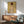 May include: Framed art print of a figure with reddish hair viewed from behind against yellow background, displayed above wooden sideboard with table lamp in modern living room setting with mint green upholstered chair and natural lighting casting shadows on white wall.