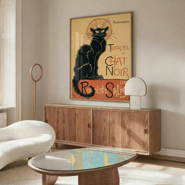 May include: Vintage French poster featuring a black cat with arched back and ornate decorative halo against cream background, displayed in thin frame above mid-century walnut credenza in modern living room with white curved chair, brass floor lamp, and glass-top coffee table on light wooden floors.