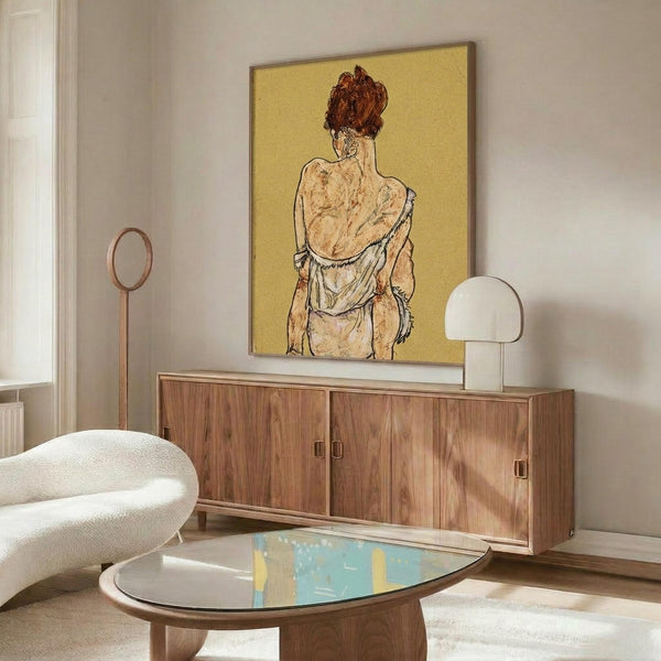 May include: Framed art print featuring a figure with reddish hair viewed from behind against yellow background, displayed on walnut credenza in modern living room with white curved chair, glass coffee table, and white table lamp. Warm natural lighting creates shadows across the minimalist interior space.
