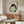 May include: Japanese-style frog artwork print in thin wood frame hanging above mid-century walnut credenza with sliding doors. Dark green frog with large white belly and red square seal stamp on cream background. Modern living room setting with white curved chair, oval glass coffee table, and warm natural lighting creating shadows on neutral walls.