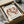 May include: Framed art print of Matisse's "The Dance" showing five red-brown figures dancing in a circle on cream background, displayed in black frame inside cardboard shipping box with white tissue paper and wooden dowels, sitting on white fabric surface next to dark glass object.
