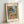 May include: Framed art print featuring Henri Matisse's colorful Mediterranean coastal scene with coral pink buildings, green shutters, palm trees, and blue water view. The vintage-style poster shows "MATISSE" at top and "VIEW OF NICE" at bottom in warm terracotta lettering. Light wood frame sits against white wall with natural lighting creating soft shadows.