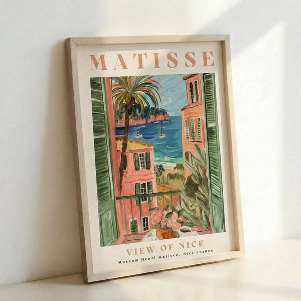 May include: Framed art print featuring Henri Matisse's colorful Mediterranean coastal scene with coral pink buildings, green shutters, palm trees, and blue water view. The vintage-style poster shows "MATISSE" at top and "VIEW OF NICE" at bottom in warm terracotta lettering. Light wood frame sits against white wall with natural lighting creating soft shadows.