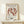 May include: Matisse "The Dance" poster in thin wooden frame on light wood shelf against cream wall. Shows five terracotta-colored dancing figures in a circle on beige background. Black text reads "MATISSE THE DANCE" and "BERGGRUEN & CIE" with Paris gallery details. Small white wrapped gift with evergreen sprig sits beside frame.