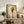 May include: Framed artwork showing pasta twirled on a black fork against a warm, textured beige background, displayed on a rustic wooden sideboard alongside books, a ceramic vase, and a fern plant in a neutral-toned living room setting with natural lighting